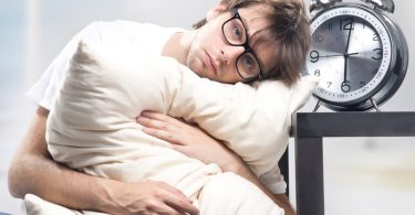 Sad man holding a pillow next to a large clock (Flickr by hang_in_there)