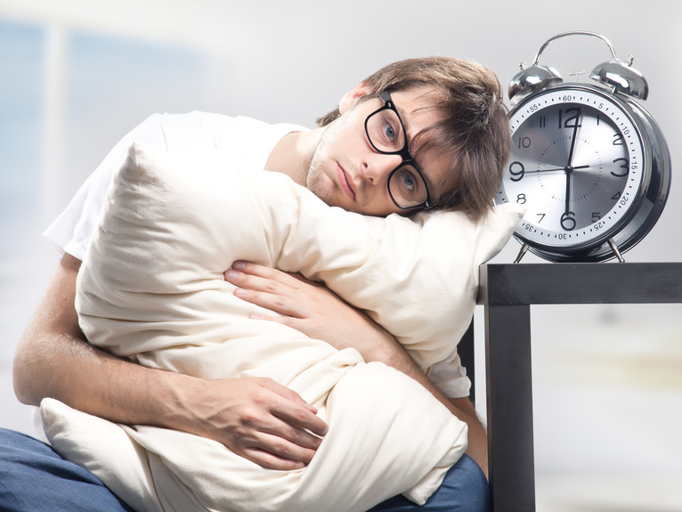 Sad man holding a pillow next to a large clock (Flickr by hang_in_there)